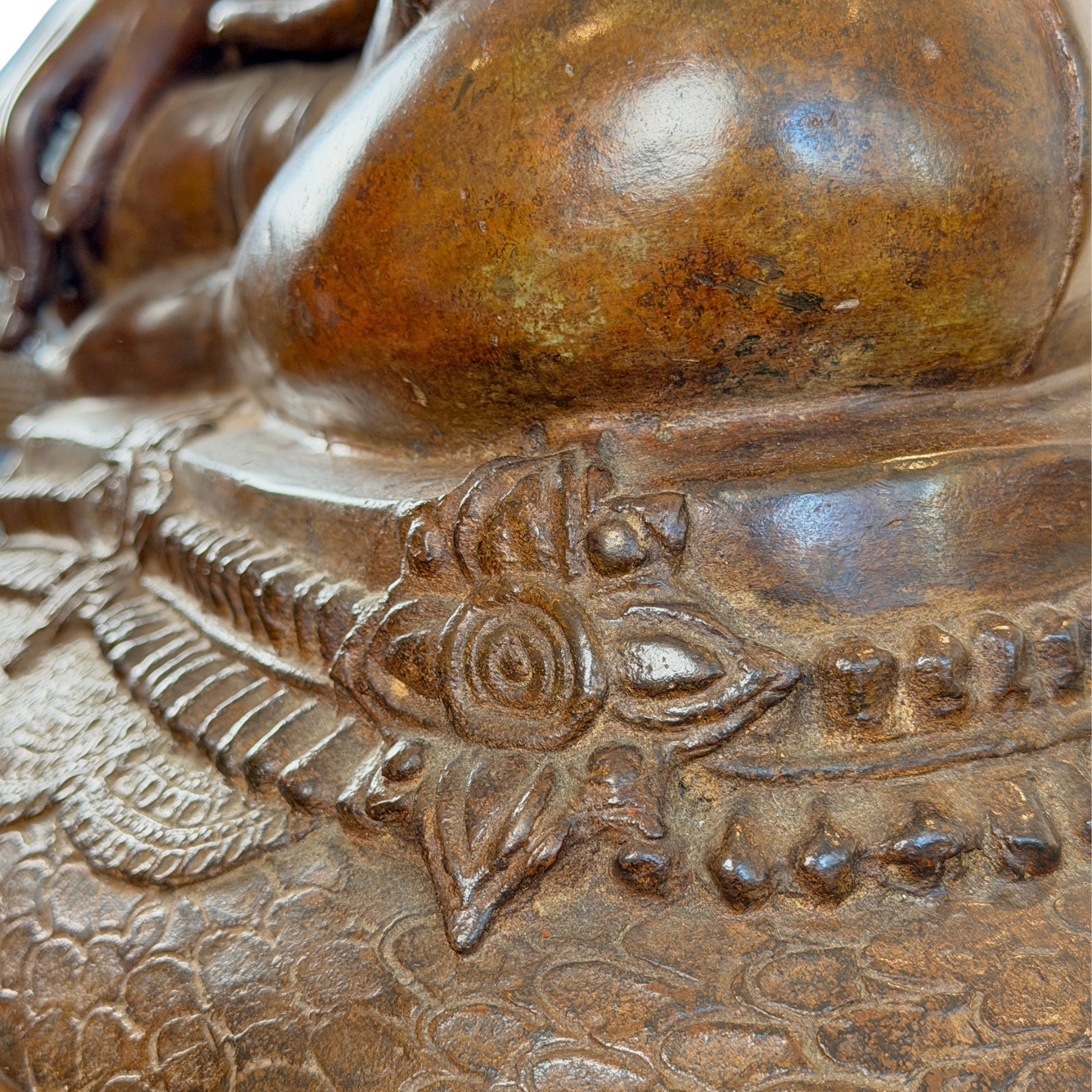 Detail der bronzenen Naga-Basis mit floralem Reliefmotiv und natürlich gewachsener goldbrauner Patina