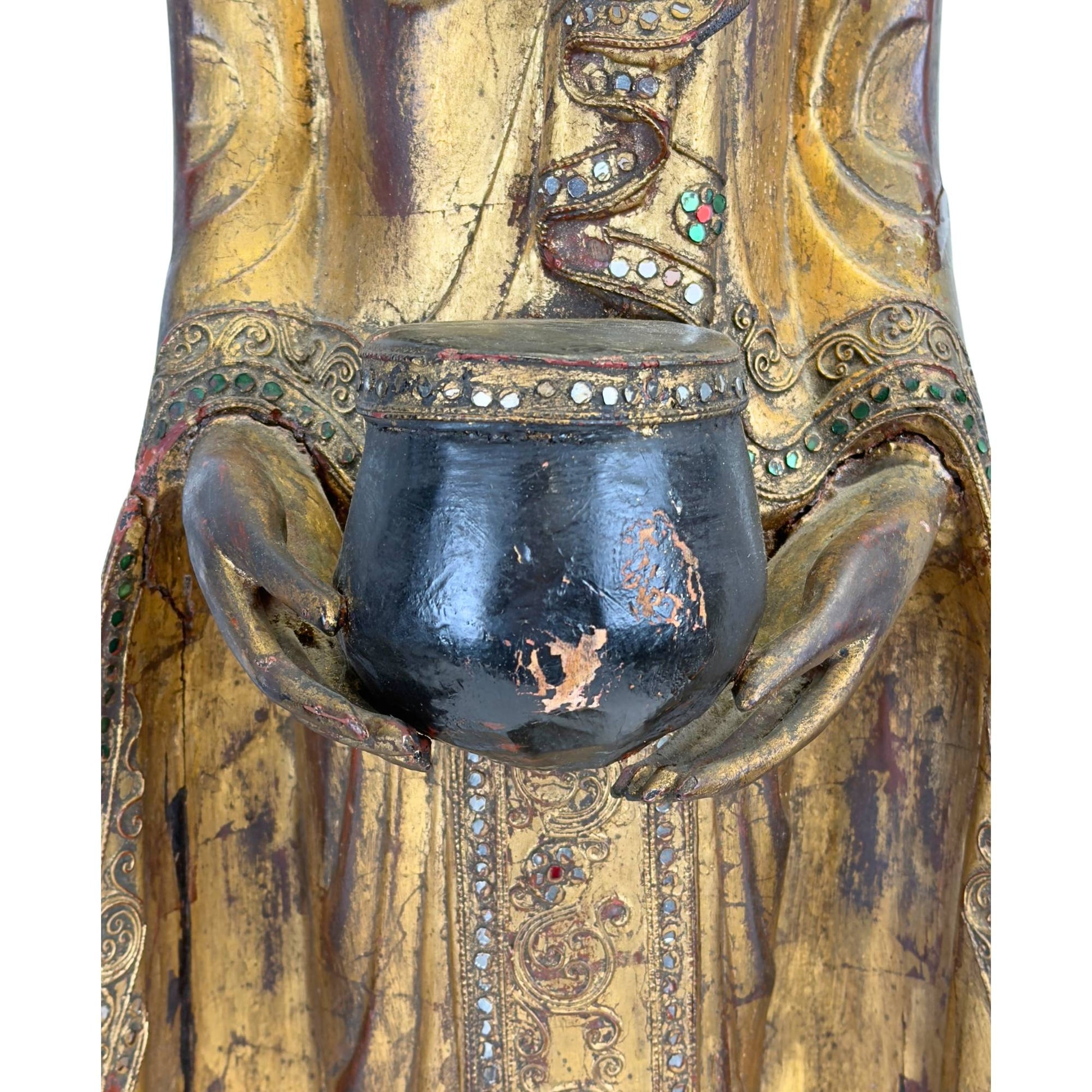Nahaufnahme der schwarz lackierten Bettelschale, die der antike Buddha trägt, mit Fokus auf die authentische Patina.