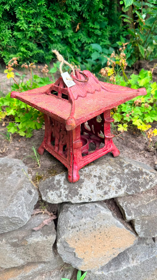 Antike japanische gusseiserne Tempellaterne mit roter Lackierung, zwischen Naturstein in einem japanischen Garten platziert.