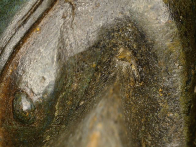 Mikroskopdetail der Brustoberfläche mit dunkler und blaugrüner Patina am antiken Bronze-Buddha
