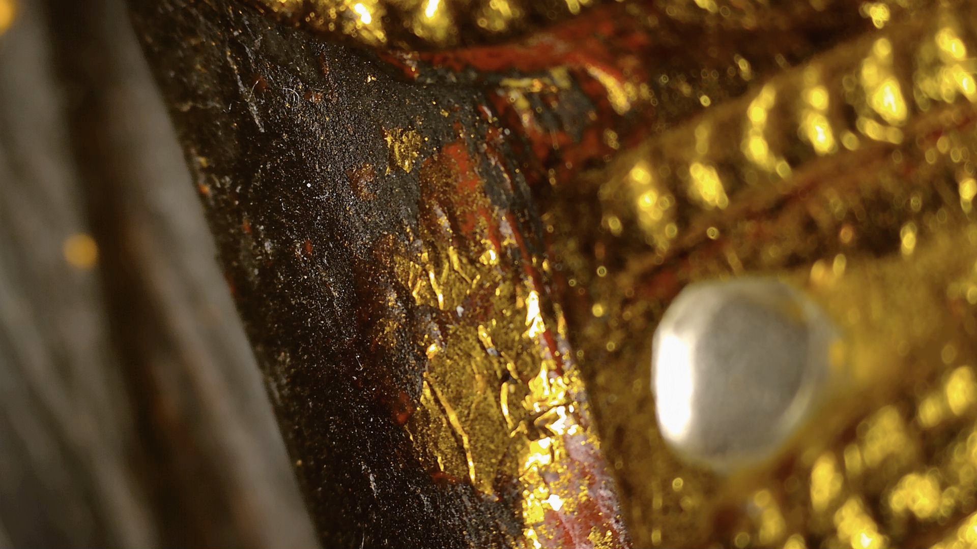 Mikroskopdetail von schwarzem Lack, rotem Untergrund und Vergoldungsresten