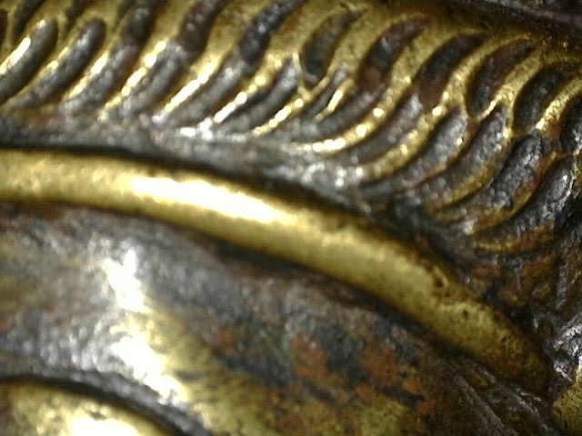 Mikroskopische Detailaufnahme der Feuervergoldung und Abnutzungsspuren an einer Brahma-Statue aus Bronze.