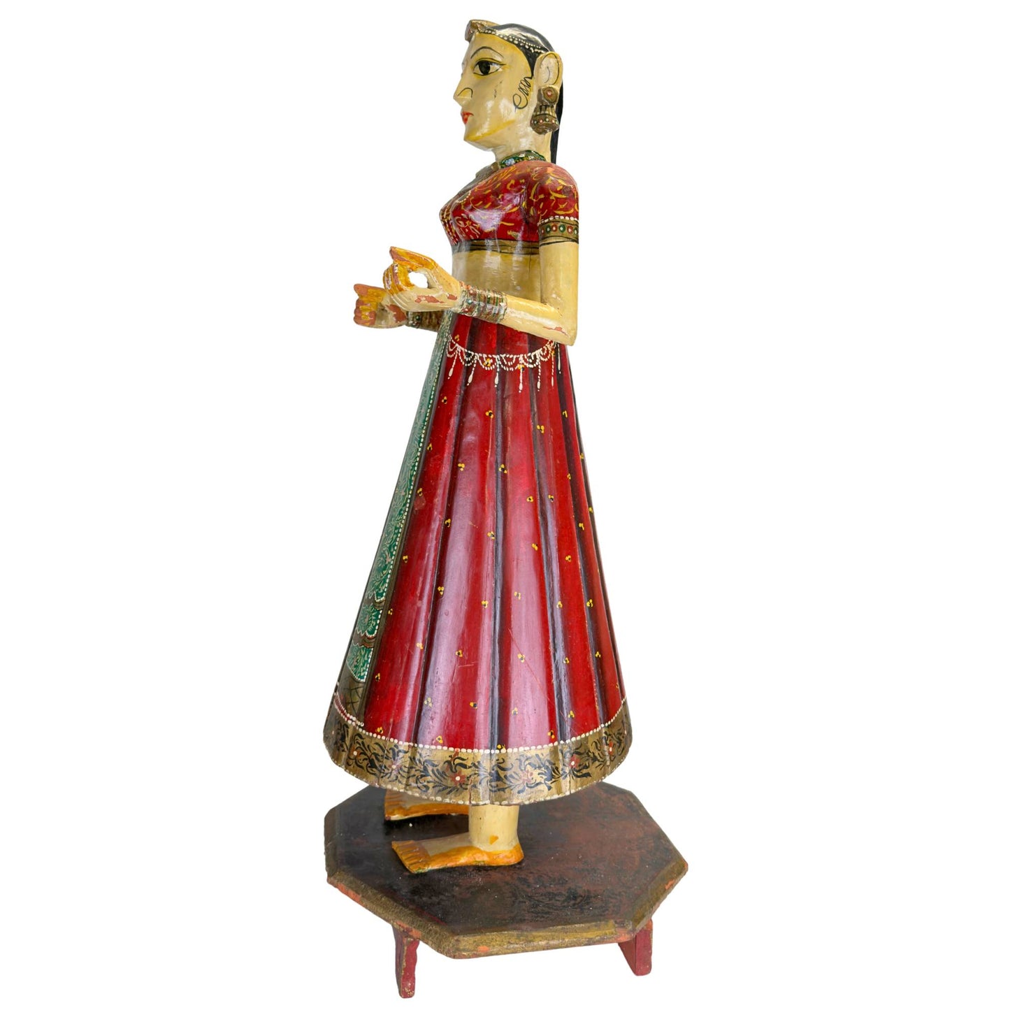 Handbemaltes Chaniya Choli-Kleidungsstück an einer indischen Holzstatue mit rotem Lack, goldfarbenen Mustern und einem grünen Streifen.