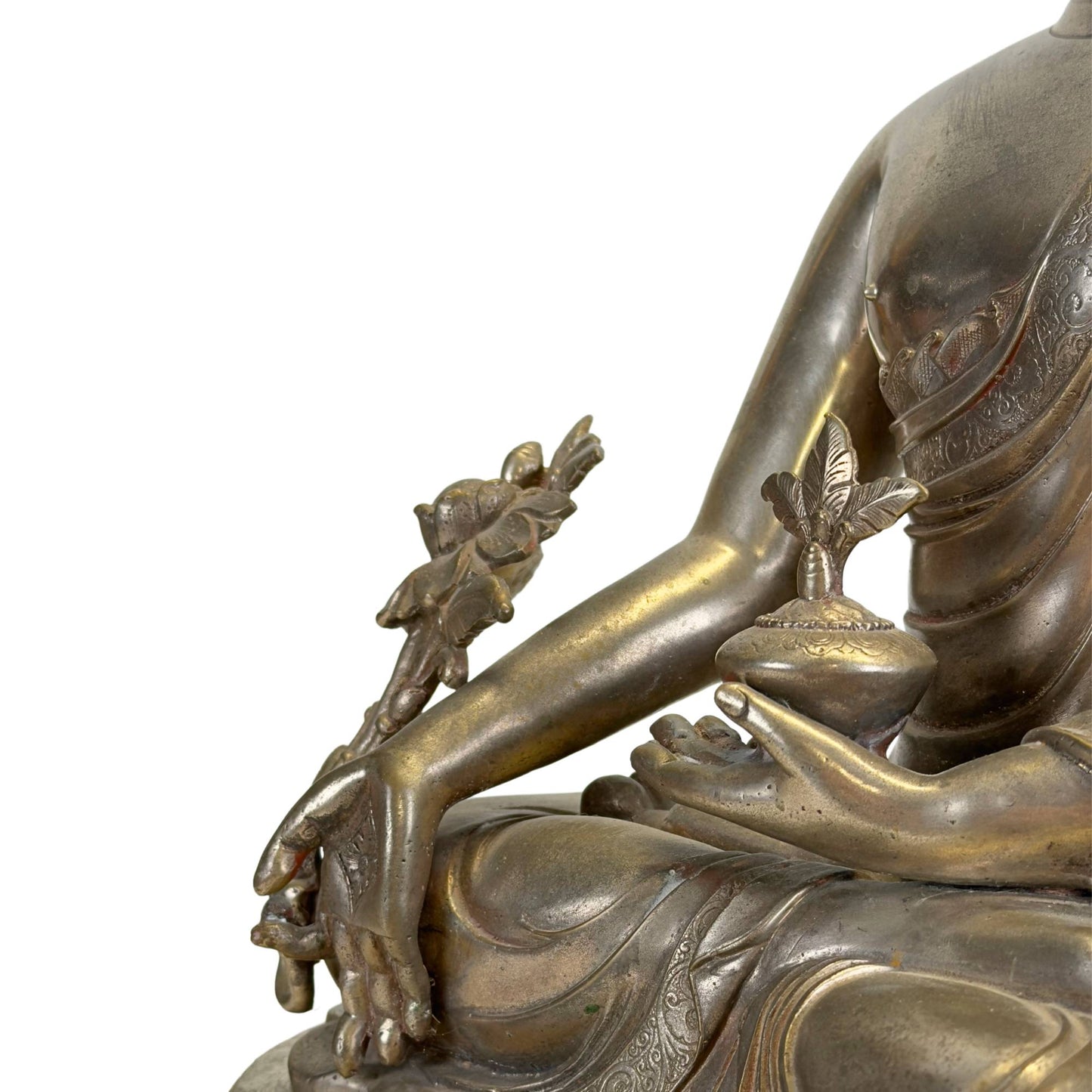 Detail einer antiken Newar Bhaisajyaguru-Figur aus versilberter Bronze mit Medizintopf, Myrobalanenpflanze, fein gravierten Gewändern und natürlichen Gebrauchsspuren, die ihr hohes Alter unterstreichen.