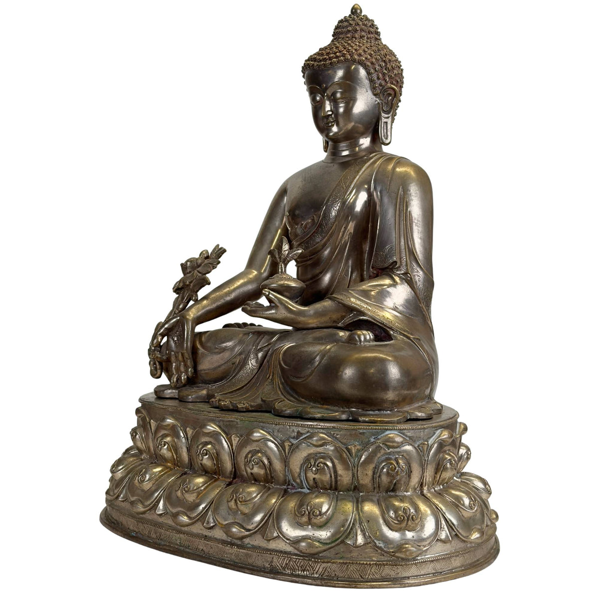 Schräge Vorderansicht einer antiken Newar Bhaisajyaguru aus versilbertem Bronze mit Medizinflasche, großer Myrobalan‑Pflanze, fein gravierten Gewändern, zweiteiliger Lotuskrone und natürlicher Patina.