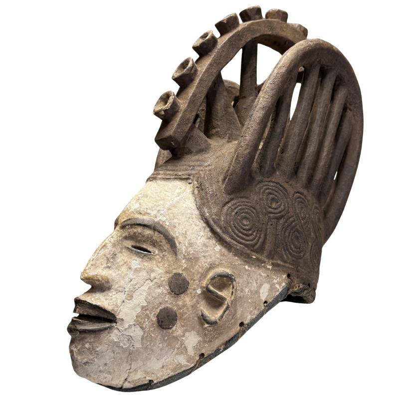 Alte afrikanische Maske mit weißer Patina, handgeschnitztes Ritualobjekt mit dunklem Kopfschmuck und spiralförmigen Verzierungen