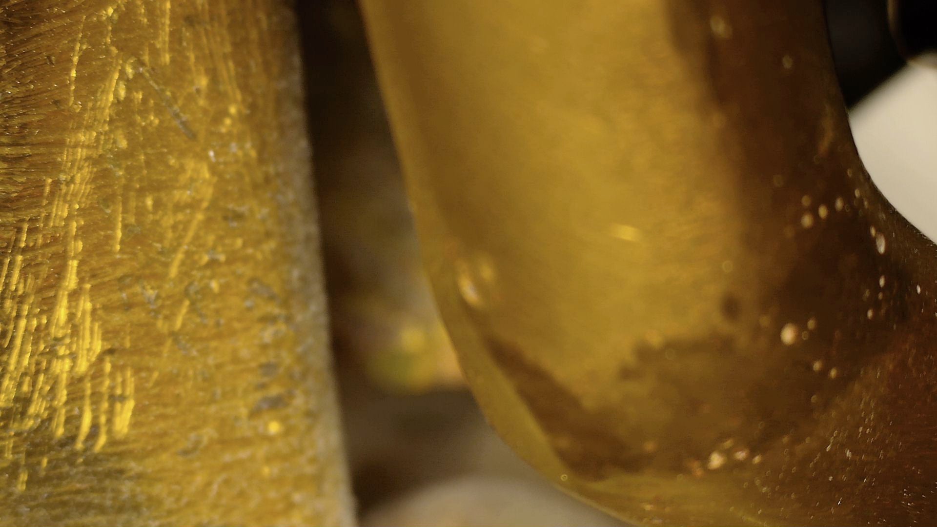 Mikroskop-Detail von alten Kratzern und brauner Patina auf antikem tibetischem Buddha.