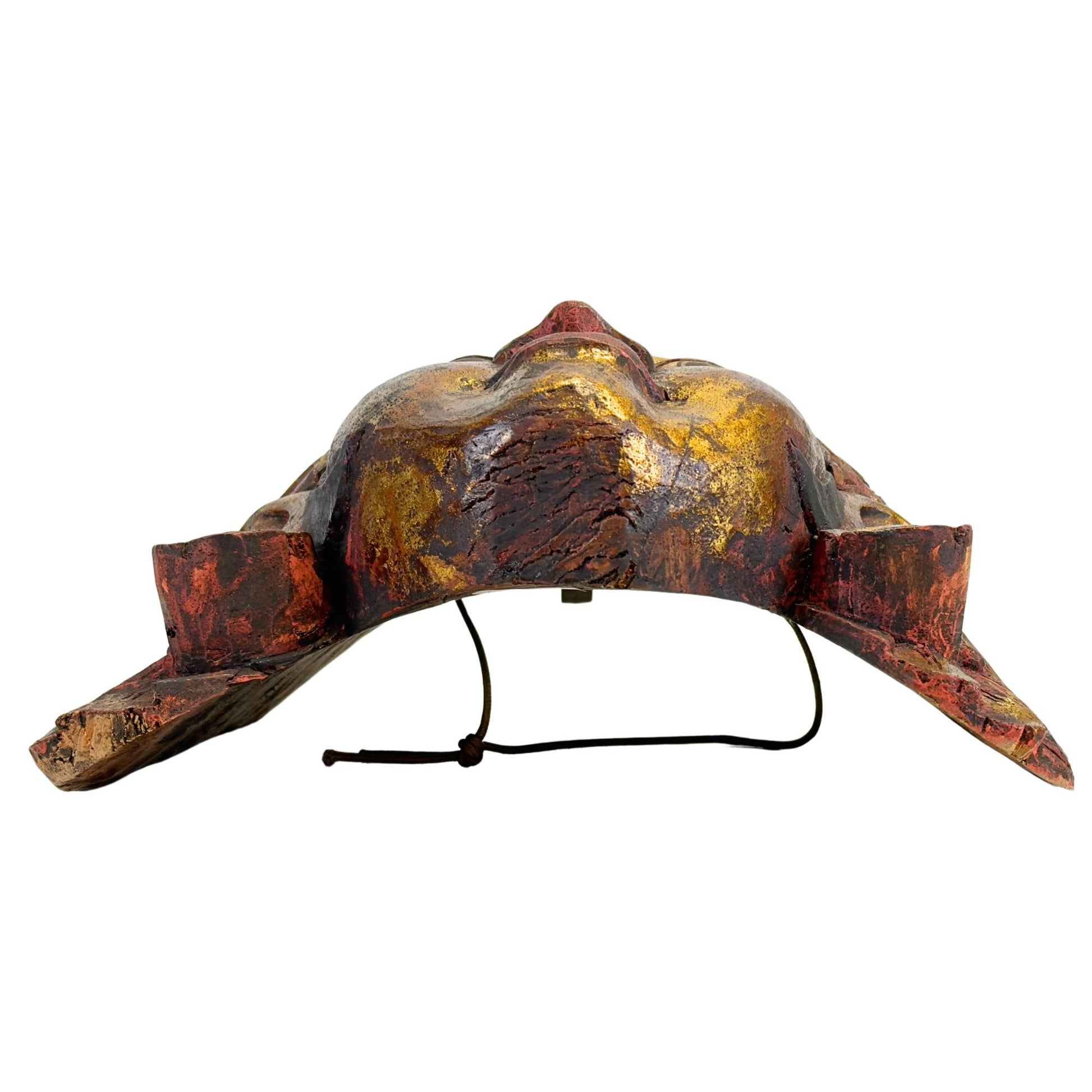 Ansicht von unten der balinesischen Topeng-Maske, wobei der Fokus auf den funktionalen, horizontalen Sehschlitzen unter den Augenlidern und der ergonomischen Aussparung für den Tänzer liegt.