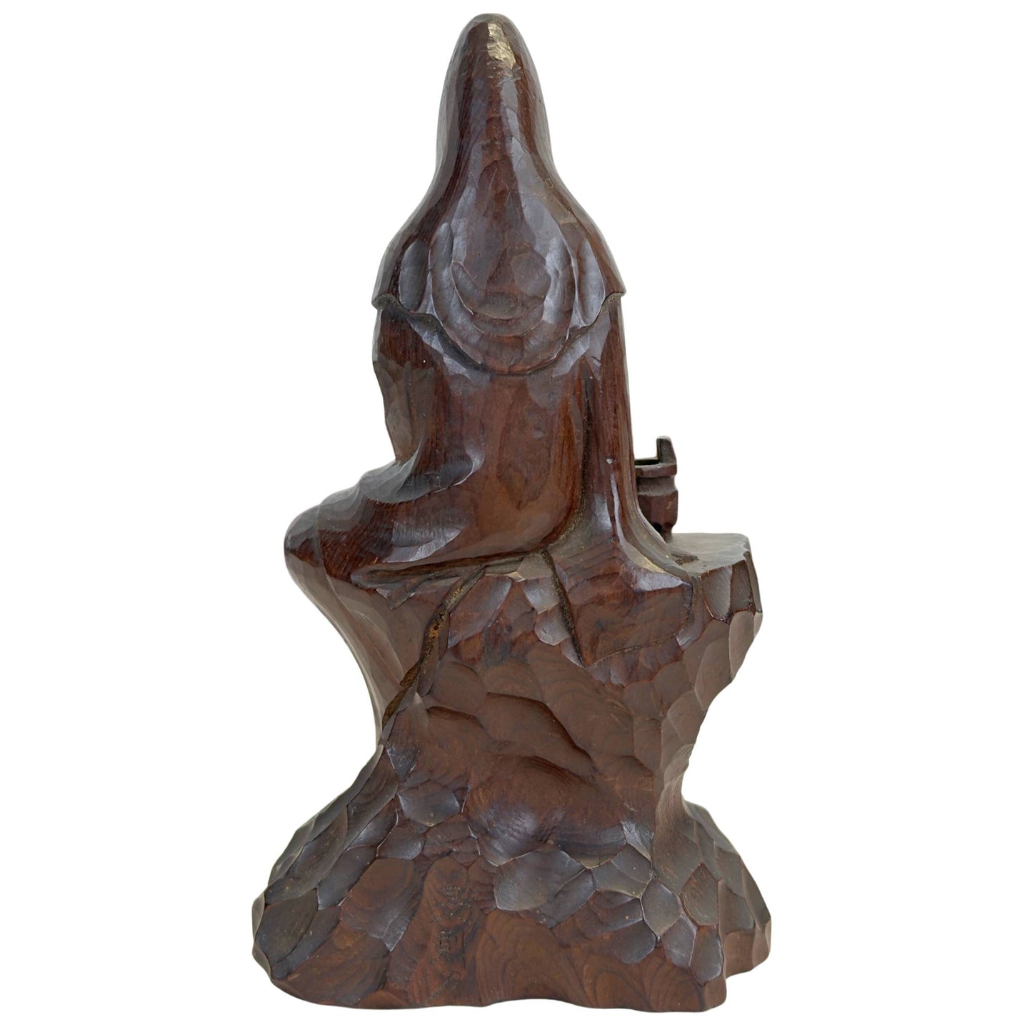 Die buddhistische Skulptur von hinten mit den geometrischen, facettierten Meißelspuren auf der Rückseite und dem sanften Glanz auf der Kopfbedeckung.